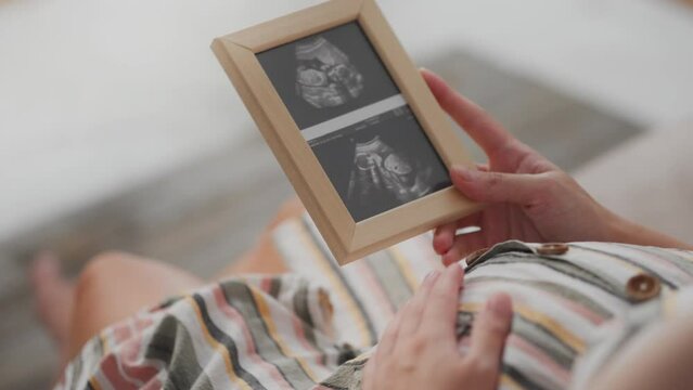 Holding on to her stomach, a housewife parent in maternity clothes examines a snapshot of the reins of her unborn child. A modern mom is holding a frame with a photo of bridles in her hands future mom