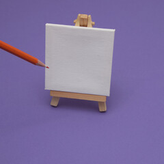 Painting canvas on a stand on a purple background with an orange crayon. Minimal painting scene.