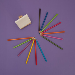 Wooden crayons of various colors on a purple background with canvas for painting. Minimalistic art paint composition.