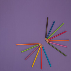 Wooden crayons of various colors on a purple background. Minimalistic art paint composition.