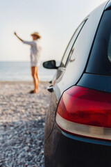 Woman traveler stands beside her car on a pebble beach and capturing the scenic beauty with her smartphone