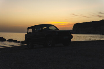 Sunset silhouette of a convertible SUV on a pebble beach