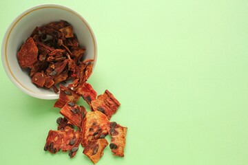 Slices of red dehydrated watermelon pulp pieces at white bowl on green background. Dried fruit chips. Organic natural healthy snack food. Homemade vegan diet. Home cooked superfood dessert.