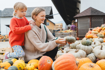 Mother and daughter choosing pumpkins at farm market at autumn season