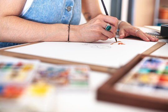 Selective focus on the hands of an illustrator painting her work among the different watercolour materials.