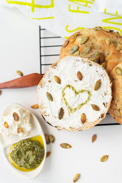 Very tasty and healthy carbohydrate breakfast. Freshly baked bagel with cream cheese, sunflower seeds and a painted heart topped with pesto sauce.