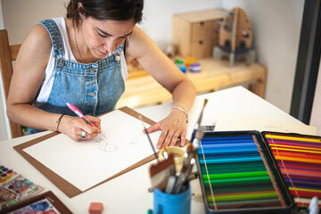 Top shot of illustrator working at her home studio table with all the material. Colored pencils,...
