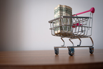Pink handle shopping cart full of one dollar bills on wooden table. One dollar bills in a shopping basket.