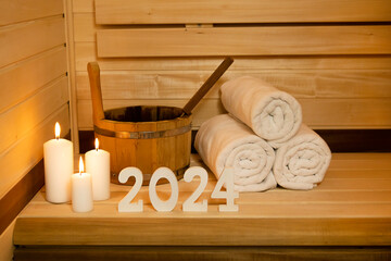 New Year card. Sauna numbers 2024 wooden white, towel ,bucket and candles. The concept of relax,...