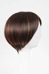 Natural looking dark brunet wig on white mannequin head. Short brown hair on the plastic wig holder isolated on white background, side view.