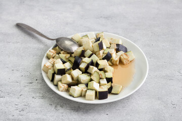 Diced eggplant on a plate sprinkled with salt on a gray textured background. The concept of cooking vegan homemade food