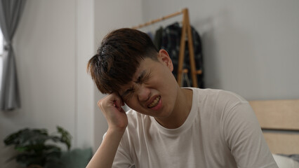 closeup shot of a tired asian male rubbing his temples with a painful look for he is having bad headache from hangover after waking up in the morning at home.