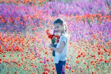 Beautiul girl holding big bouquet with poppies on the background of a colorful spring field