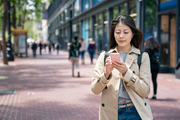 Fototapeta premium asian Japanese female traveler searching for travel information on the phone in the breeze while walking on the sidewalk in the financial district of san Francisco in California usa