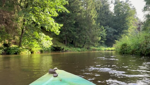 Kayaking on a river in Summer. Focus on kayak's boat bow or front side part. Beautiful scenery river with calm water route along green forest. No people. Watersport and recreational activity concept.