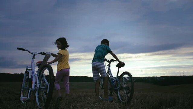 Golden Hour Bliss: Young Boy and Girl Embrace on Bicycles in the Elevated Evening Field