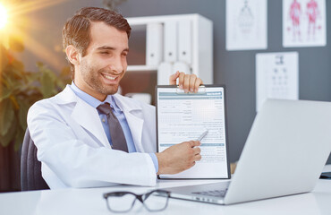 Close up of a doctor and patient hands while phisician pointing into medical history form at clipboard