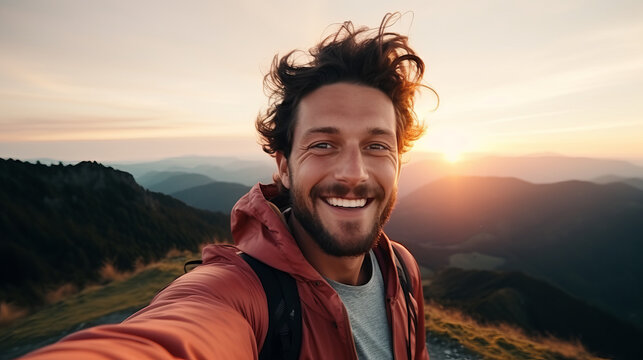 Selfie picture of a young hiker man at top of mountain , happy caucasian guy smiling at camera and enjoying the sunset view