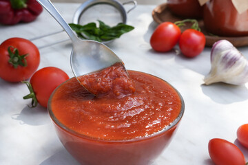 Close up of ketchup and tomatoes placed on a lght marble background. Scoop ketchup with a spoon. Side view. 