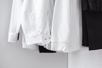 A close-up of the sleeves and cuffs of white clean shirts hanging in the closet. Black trousers in...