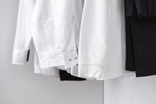 A close-up of the sleeves and cuffs of white clean shirts hanging in the closet. Black trousers in the wardrobe. Classic style clothes. Whitening. Office style. School uniform