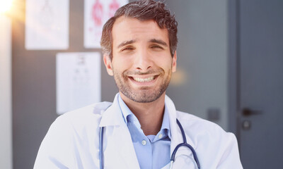 male nurse with stethoscope standing at clinic. He is smiling and looking at the camera.