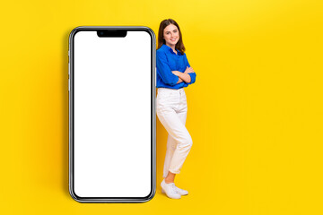 Full length photo of cute pretty girl dressed blue shirt arms folded modern device empty space isolated yellow color background