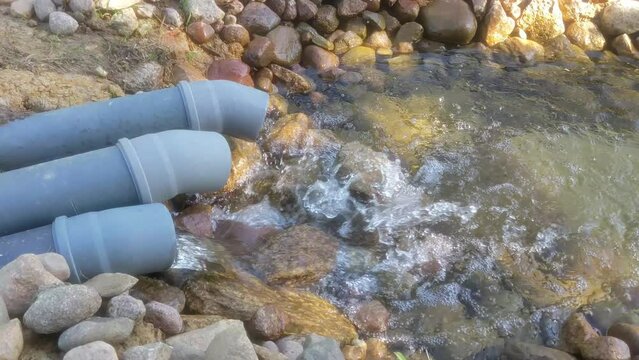 Fresh drinking water from the artesian well comes through a water pipe. A stream of sewage flows out of a plastic sewer pipe into the river.