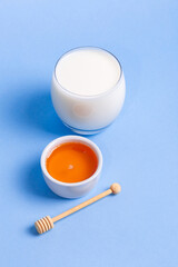 Glass of milk and bowl of honey on blue background.
