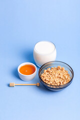 Glass bowl of granola, glass of milk and honey on blue background. Healthy and tasty breakfast.