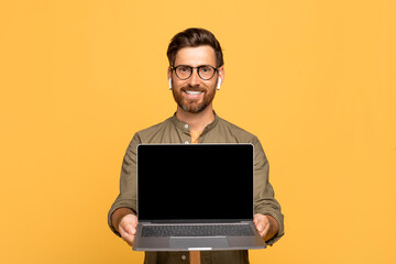 Positive middle aged man showing modern laptop with black empty screen, mockup for online offer, app, website advert