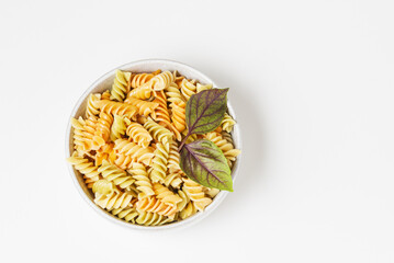 Spiral colored fusilli pasta with fresh basil leaves in ceramic bowl isolated on white background with copy space top view
