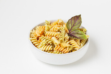 Spiral colored twisted pasta with fresh basil leaves in ceramic bowl isolated on white background 