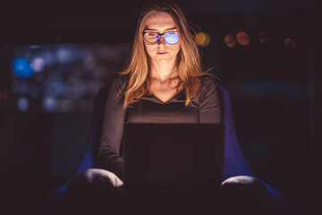 Laptop on woman's lap. A face illuminated by a laptop display. Work at night.