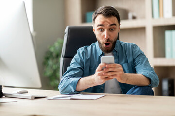 Amazing Offer. Portrait Of Shocked Man Looking At Smartphone Screen In Office