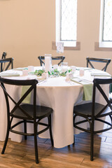 An elegantly decorated table for a wedding. Black chairs surround a white tablecloth table with green napkins, candles, and greenery. 