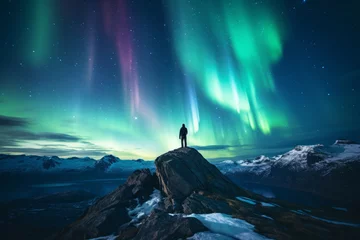 Poster Im Rahmen Silhouette of a man standing on the top of a mountain admiring the view of aurora borealis. Sky with stars and green polar lights. Northern lights. © MNStudio