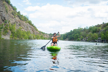 A 10-year-old boy rides a SUP board alone on a mountain lake, river, canyon. a child on a summer vacation studying rides a stand-up board on a trip in nature.