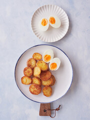 Plate of crispy, golden brown roasted potatoes with hard boiled egg. Another plate with halved egg. Top view on blue background.