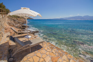 Shore of the turquoise mediterranean sea at the island of Crete, Greece, near Agios Nikolaos, with sunshade parasol, rocky coast