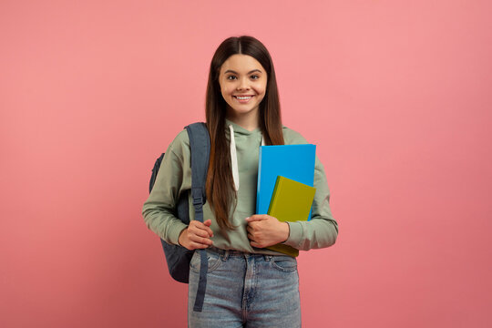 Portrait of happy young female student with backpack and books posing over pink studio background