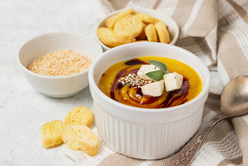 Pumpkin soup puree with sauce,  soy cheese and sesame seeds  and toasts in a white bowl  on a light table napkin