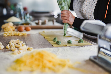 Senior woman preparing fresh made ravioli with ricotta cheese and spinach inside pasta factory -...