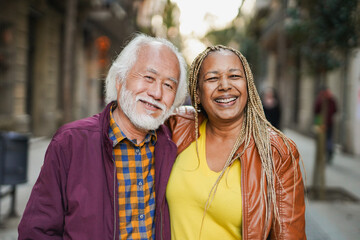Multiracial senior couple smiling on camera during city trip vacation with street in background