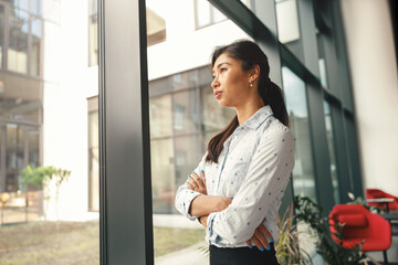 Attractive business woman standing with crossed hands and smile in office while looking at side