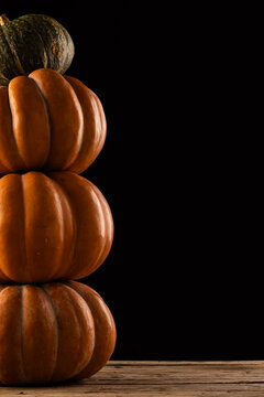 Vertical image of orange and green pumpkins stacked up with copy space on black background