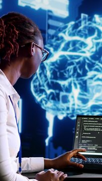 Vertical video African american IT expert updating AI systems, writing intricate binary code scripts on tablet and laptop. Certified admin using programming to upgrade artificial intelligence
