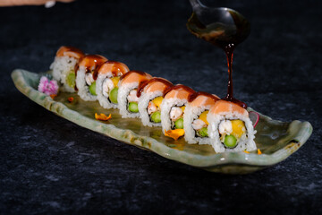 Crop person pouring sauce with spoon on sushi with salmon and vegetable on tray