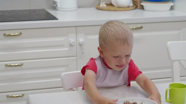 mother tries to feed the child with porridge, the baby refuses to eat pushing the plate away