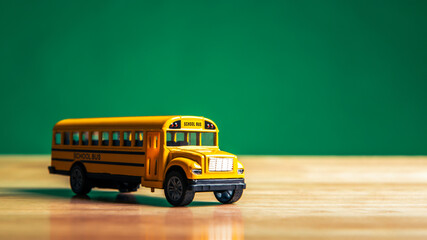 Yellow school bus model on the student table with chalkboard or blackboard background....